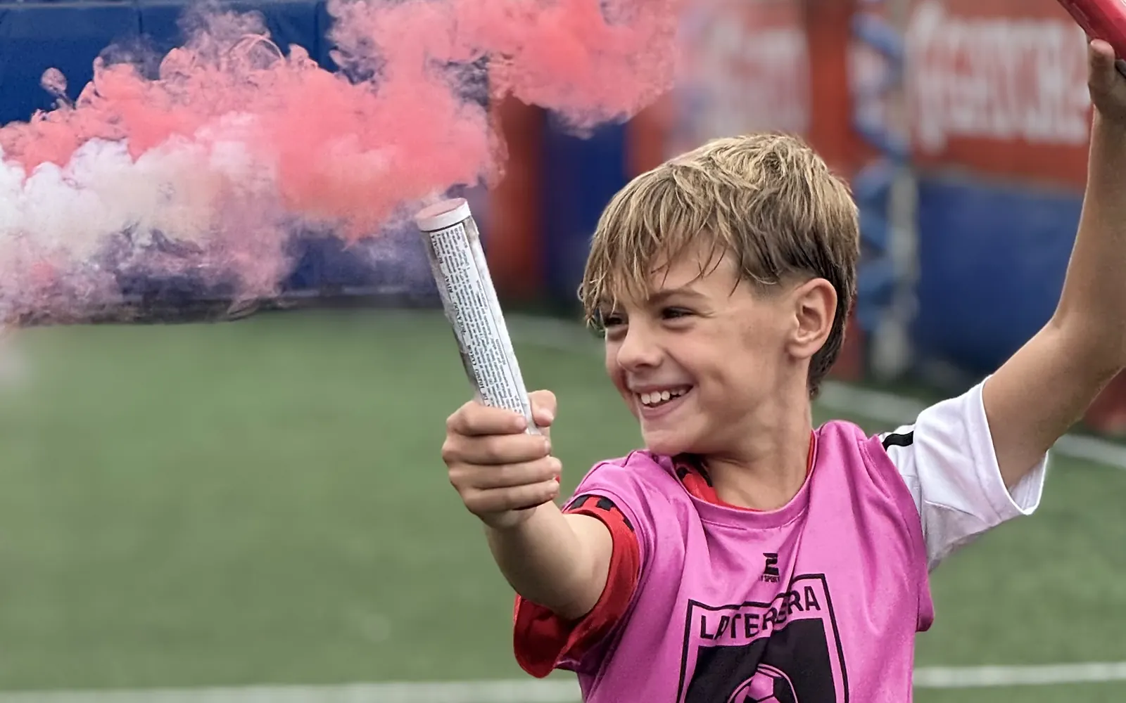 Un chico del cumple sonriendo con una bengala de humo rosa en la mano